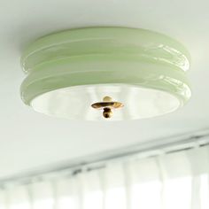 a green light fixture hanging from the ceiling in a room with white walls and windows