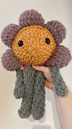 a hand holding up a crocheted flower with two black eyes and one brown eye