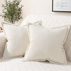 two white pillows sitting on top of a bed next to a plant in a vase