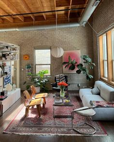 a living room filled with furniture and lots of windows next to a brick wall covered in plants