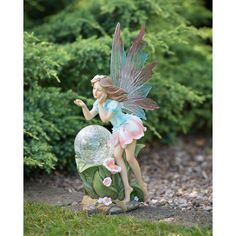 a fairy figurine sitting on top of a rock in front of some bushes