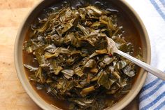 a bowl filled with cooked collard greens on top of a wooden table next to a blue and white towel