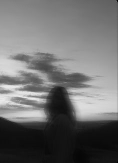 a blurry photo of a woman walking in the grass with her hair blowing in the wind