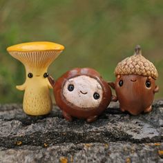 three little figurines sitting on top of a rock next to a mushroom and an acorn