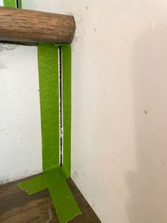 the corner of a room with a piece of green tape and a wooden stick sticking out of it