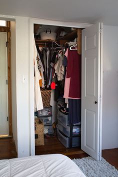 an open closet with clothes and other items on the shelves in front of it, next to a bed