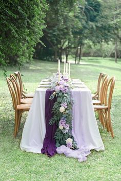 the table is set with purple flowers and greenery on it, along with candles