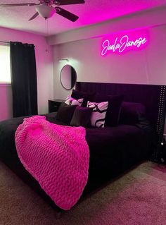 a bedroom with pink lighting and black bed in the center, along with a neon sign on the wall