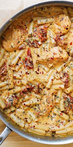 a skillet filled with pasta and meat covered in sauce on top of a wooden table