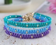 three different colored bracelets sitting on top of a white table next to a pink flower