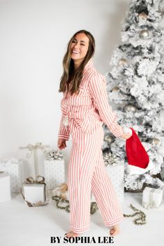 a woman standing in front of a christmas tree wearing red and white striped pajama