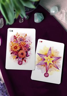 two cards with flowers on them sitting next to some rocks and crystals in the background