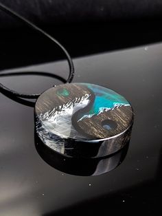 a black and silver necklace with an image of a mountain range on it's side