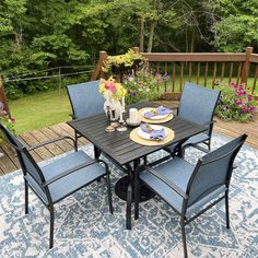 an outdoor dining table with blue chairs and plates on it in the middle of a deck