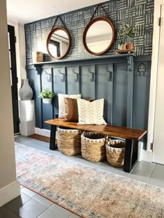 a bench with baskets and mirrors on it in front of a wallpapered entryway