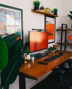 a desk with a computer monitor, keyboard and plant on it in an office setting