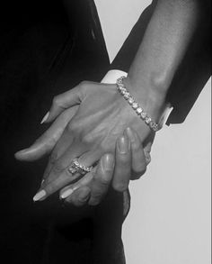 two people are holding hands with each other in black and white, one is wearing a diamond bracelet