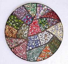 a circular piece of art made out of various colored glass tiles on a white wall