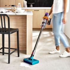 a woman is cleaning the floor in her kitchen with a multicolored vacuum cleaner