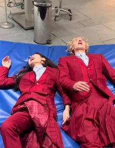 two people in red suits are laying on a blue tarp and one person has their eyes closed