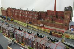 a model train set is shown in front of a building with many windows and red brick buildings