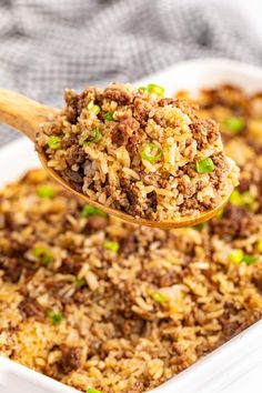 a spoon full of rice and ground beef in a casserole dish with green onions