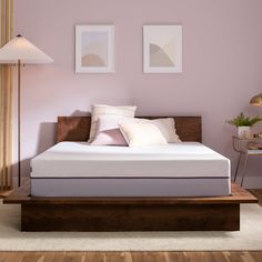 a bed in a room with pink walls and wooden furniture on the floor, along with two framed pictures