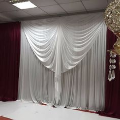 an empty room with curtains and chandelier hanging from the ceiling in front of it