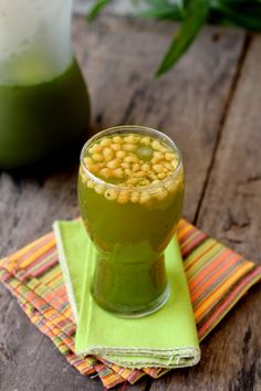 a glass filled with green liquid on top of a wooden table next to a napkin