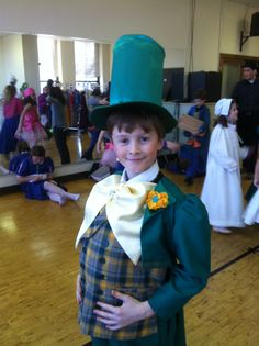 a young boy dressed up in a green top hat and bow tie, standing on a hard wood floor