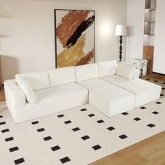 a large white couch sitting on top of a wooden floor next to a painting in a living room