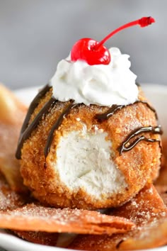 a pastry with whipped cream and a cherry on top sits in a white bowl surrounded by chips