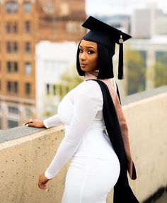 a woman wearing a graduation cap and gown leaning against a wall with her hand on her hip