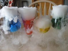 three glasses filled with liquid sitting on top of a white table next to a wooden chair