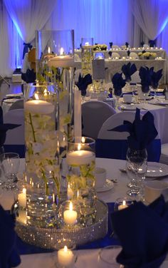 a tall vase filled with lots of white flowers and lit candles on top of a table