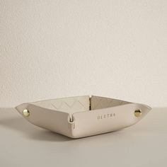 a white ceramic bowl with gold handles on a gray table top, in the shape of a boat