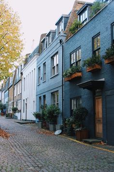 a cobblestone street lined with row houses and potted plants on the windows