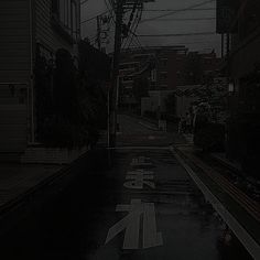 an empty street with buildings and power lines in the background on a rainy day at night