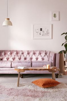 a living room with a pink couch and coffee table in front of the couch is an orange throw pillow