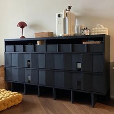 a black cabinet sitting on top of a hard wood floor next to a yellow ottoman