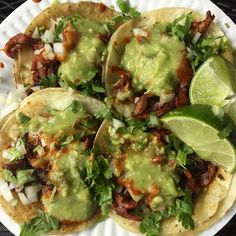 three tacos on a paper plate with avocado and cilantro