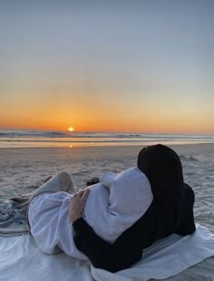 a woman laying on top of a beach covered in a blanket next to the ocean