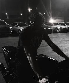 black and white photograph of a person on a motorcycle at night with cars in the background