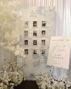 a welcome sign next to some flowers and pictures on a wall with white drapes