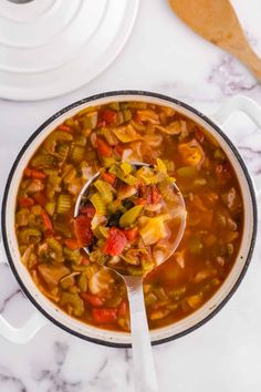 a spoon full of vegetable soup on top of a white table with utensils