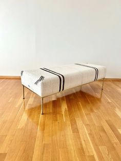 a white and black bench sitting on top of a hard wood floor next to a wall