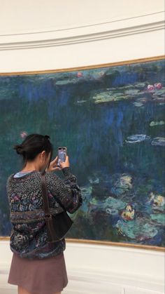 a woman taking a photo of a painting with her cell phone while standing in front of it