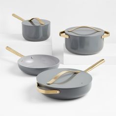 three pans with gold handles and one has a lid on the bottom, two are grey