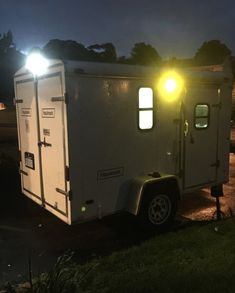 a small white trailer parked on the side of a road at night with its lights on