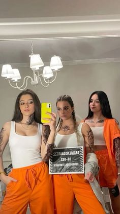 three women in orange pants are holding up a cell phone